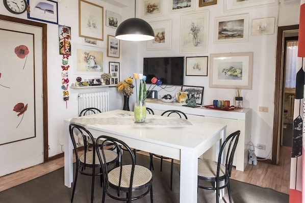 A dining area with a white table, black chairs, a black pendant light, and a wall decorated with framed pictures.