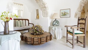 A room with a round wooden coffee table, a wooden chair, a sofa, a lamp, and a vase with flowers.