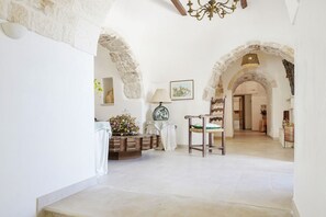 Un pasillo espacioso con arcos de piedra, una silla de madera, una lámpara y un florero con flores.