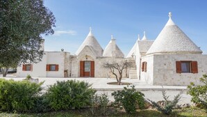 A row of white buildings with conical roofs, a stone pathway, and greenery in the foreground.