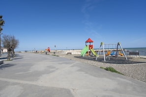 A playground with swings and slides, a bench, and a view of the beach.