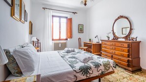 A bedroom with a bed, dresser, desk, chair, and a large mirror.
