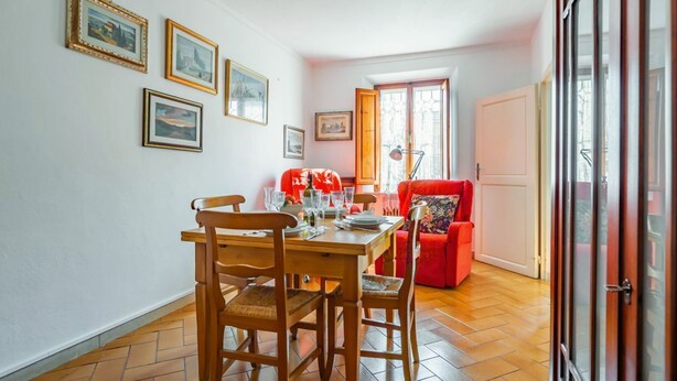 A dining area with a wooden table and chairs, a red sofa, and framed pictures on the wall.