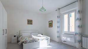 Ett sovrum med en säng, sängbord, en hängande lampa och ett fönster med gardiner.