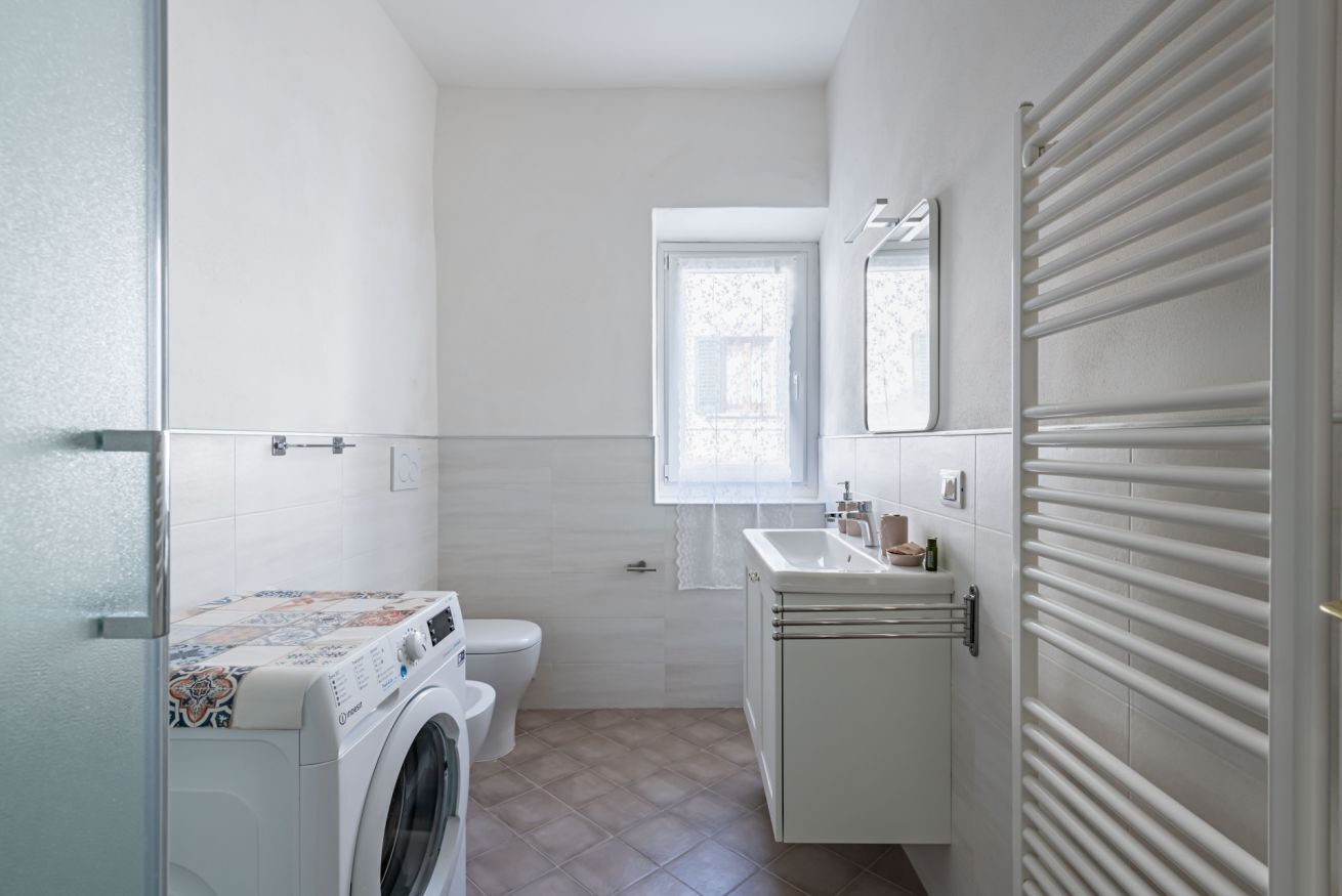A compact bathroom with a washing machine, toilet, sink, and a window.