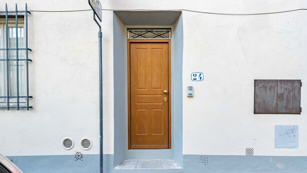 A building with a wooden door, a number 24 sign, a window with bars, and a small vent.