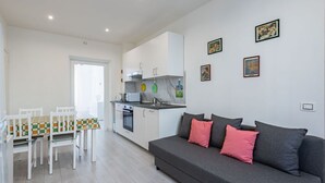 A modern kitchen with white cabinets, a dining table with chairs, and a grey sofa with pink cushions.