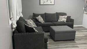 Un salon moderne avec des canapés gris et un pouf, une œuvre d’art représentant une carte du monde accrochée au mur, et un plancher en bois.