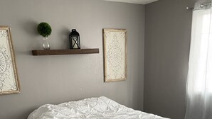 Une chambre à coucher avec un lit, une étagère en bois ornée d’objets décoratifs, un tapis à motifs et un mur gris.