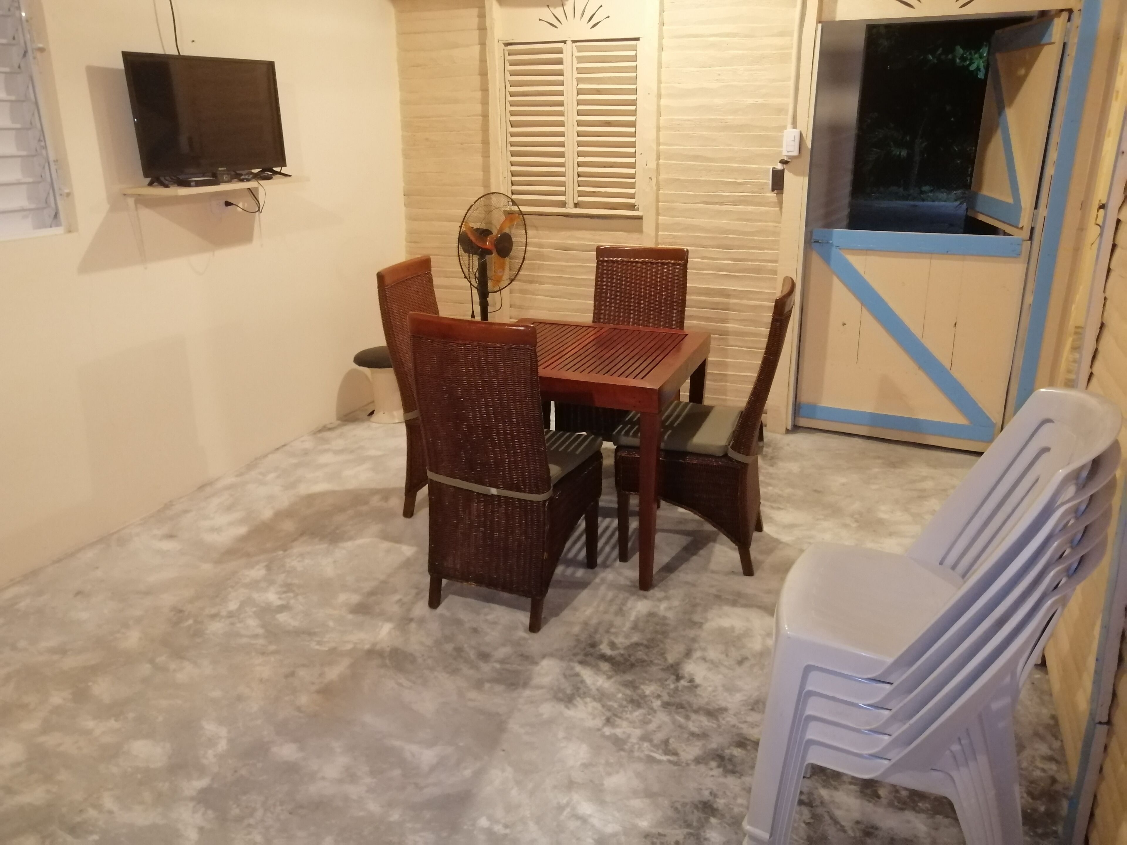 A dining area with a table and chairs, a television mounted on the wall, and a window with shutters.