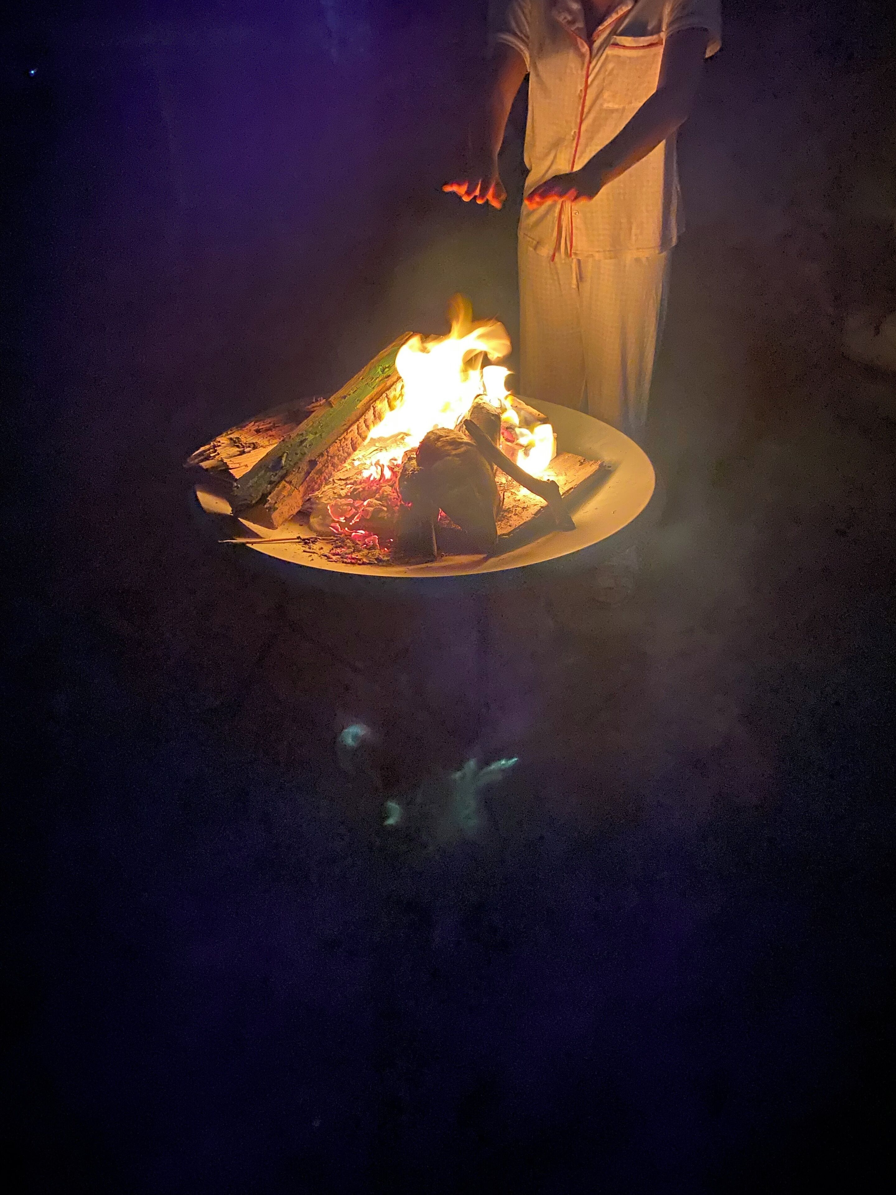 A person standing near a campfire with logs and embers.