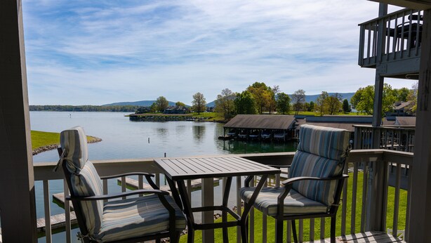 A deck with two chairs and a table overlooking a lake, with a covered area and dock in the background.