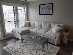 A living room with a beige sofa, a coffee table, a patterned rug, and a framed map on the wall.