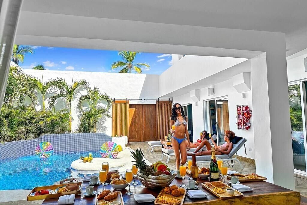 Un coin petit-déjeuner aménagé au bord de la piscine, avec une table, des boissons et des plantes tropicales.
