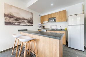 A modern kitchen with a central island, bar stools, a microwave, a refrigerator, and a painting on the wall.