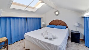 A hotel room with a large bed, a skylight, a mirror on the wall, and a small table with a lamp. - Duplex Cigarra - Welkeys (Bandol)