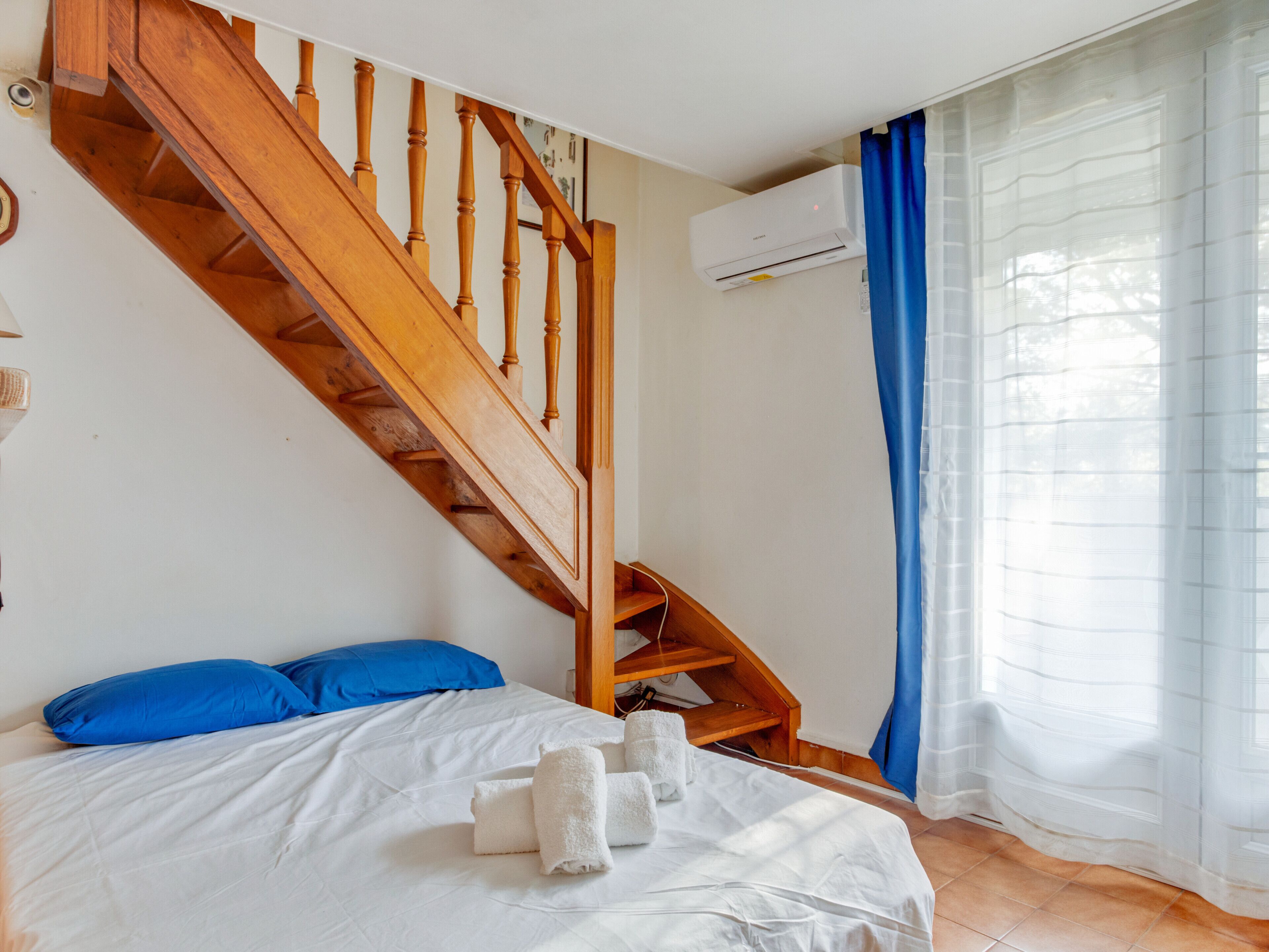 A bedroom with a wooden staircase, a bed with white bedding, blue pillows, and a set of towels.