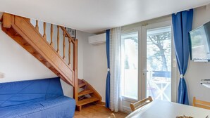 A room with a wooden staircase, a blue sofa, a dining table, and a window with curtains. - Duplex Cigarra - Welkeys (Bandol)