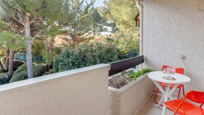 A balcony with a white table and two orange chairs, overlooking a garden with trees and a building in the background. - Duplex Cigarra - Welkeys (Bandol)