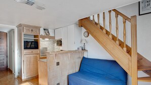 A compact living space with a kitchenette, a blue sofa, and a wooden staircase. - Duplex Cigarra - Welkeys (Bandol)