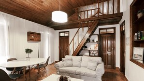 Una sala de estar acogedora con una escalera de madera, un sofá blanco, una mesa de comedor y una lámpara colgante.