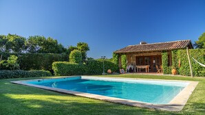 Una piscina rectangular con solárium empedrado, rodeada de césped cuidado.