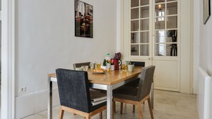 A dining area with a wooden table and four chairs, a small table with a plate of food, drinks, and a kettle.