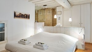 A neatly made bed with towels, a wooden floor, a white wall with a painting, and a wooden ceiling.