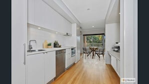 Una cocina moderna con armarios blancos, lavavajillas y horno. Hay una zona de comedor con una mesa y sillas.