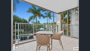 Balcón con vista a la piscina, barandilla blanca y sillones de mimbre.