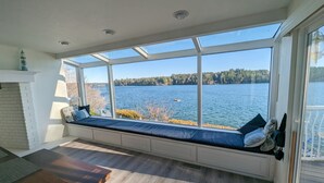 Un ventanal con vistas a un lago, un banco empotrado con cojines y una mesa de madera.