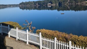 Un lago sereno con una cerca blanca en primer plano, agua tranquila y una orilla boscosa al fondo.