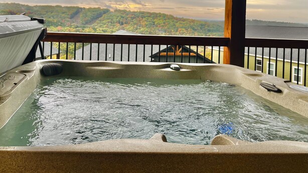 Uma banheira de hidromassagem numa varanda com vista para uma floresta e um corpo de água.