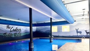Piscina interna com um mural de montanhas e veados, um posto de salva-vidas e área da piscina transparente.