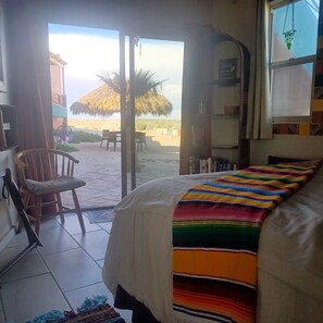 Una habitación con cama, una silla, una estantería y vista a la playa.