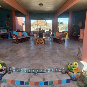 Un amplio espacio al aire libre con mobiliario de mimbre, una mesa central y elementos decorativos en las paredes.