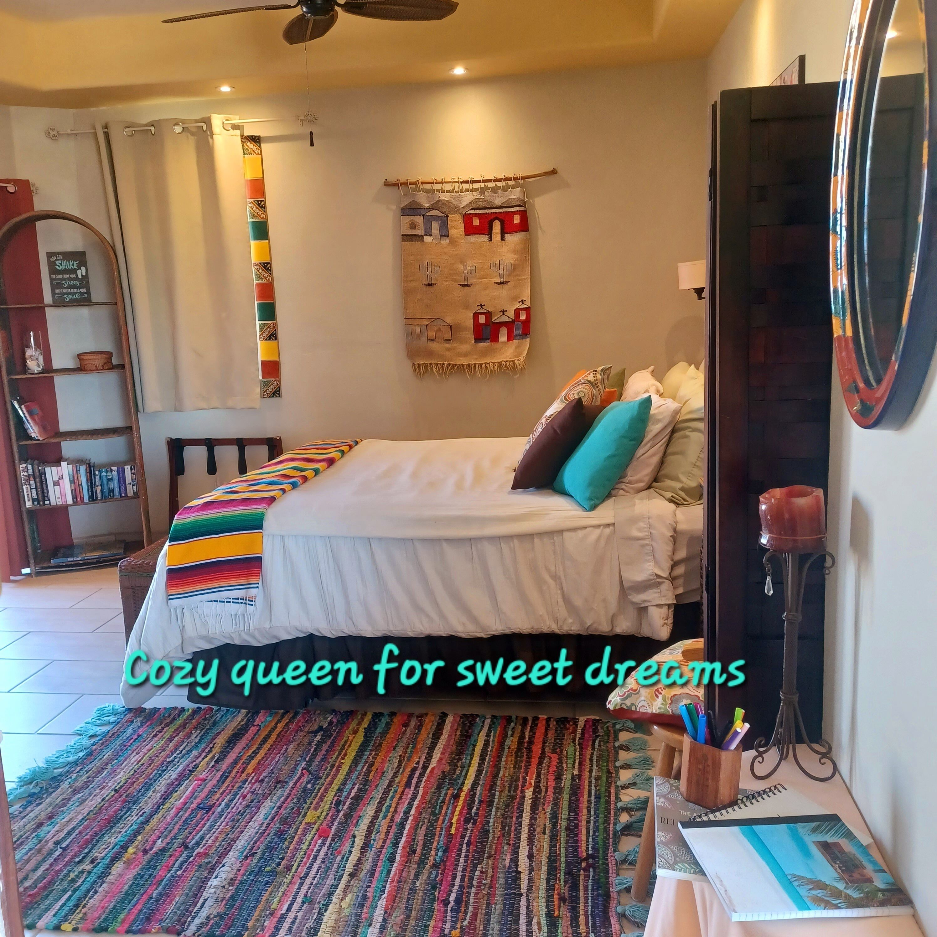A cozy bedroom with a bed, colorful pillows, a rug, a bookshelf, and a wall tapestry.