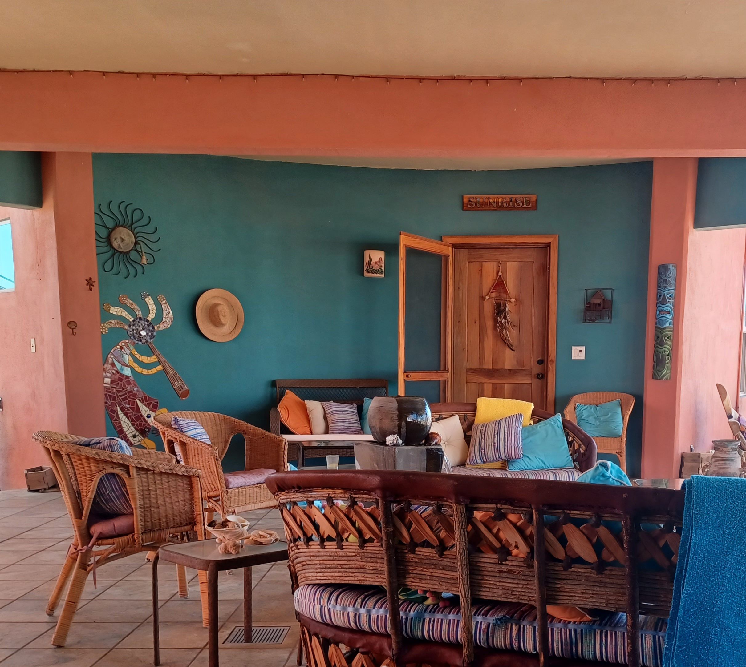 A cozy outdoor seating area with wicker furniture and a wooden table, set against a teal wall with decorative elements.