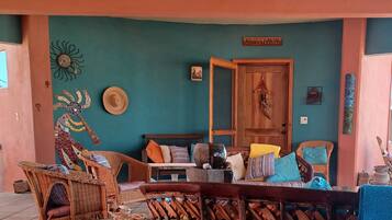 A cozy outdoor seating area with wicker furniture and a wooden table, set against a teal wall with decorative elements.