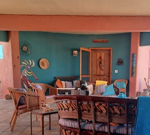 Cómoda zona de estar al aire libre con mobiliario de mimbre y una mesa de madera, frente a una pared verde agua con detalles decorativos.