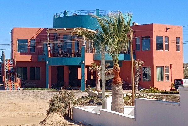 Un edificio con fachada azul y roja, un balcón y palmeras al frente.
