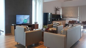 A modern living room with a flat-screen TV, comfortable seating, a kitchen area, and a dining space.