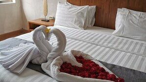 A neatly made bed with white pillows and a striped bedspread, a wooden nightstand with a decorative item, and a window with curtains.