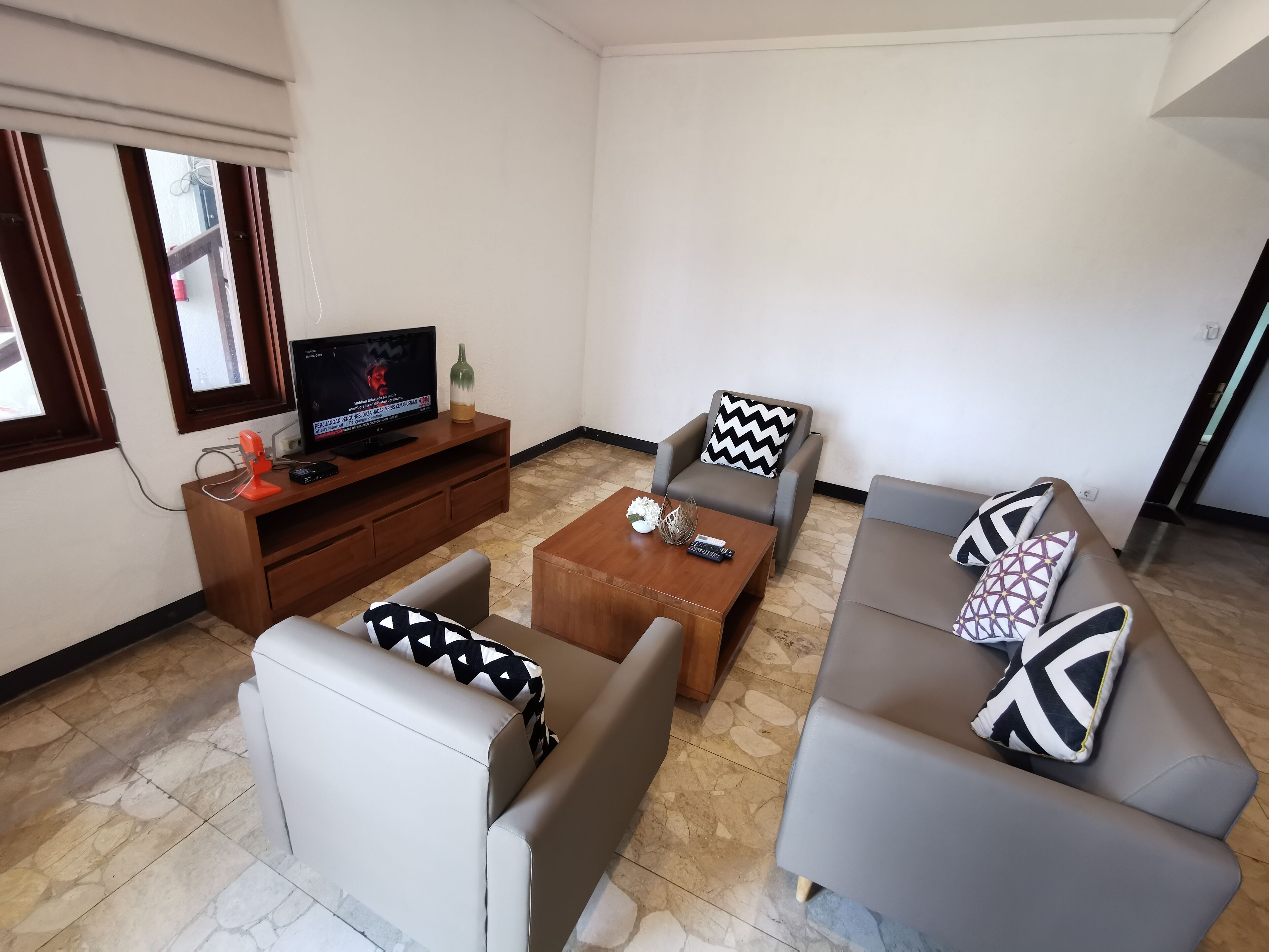 Een woonkamer met een televisie, bank, salontafel en een gestreept kussen.