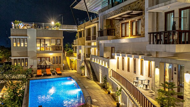 A modern multi-story building with a swimming pool, outdoor seating, and a balcony with a view.