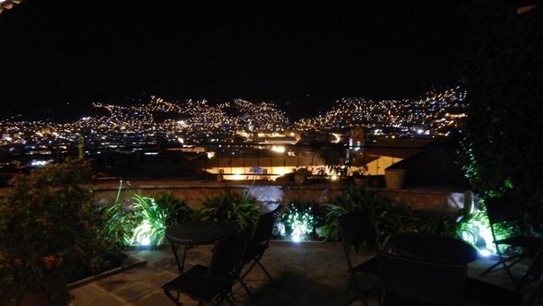 An outdoor patio area with chairs and tables, overlooking a cityscape at night.
