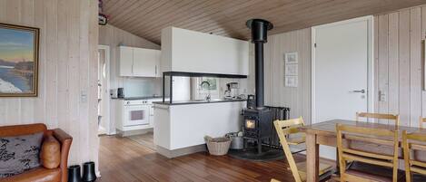 A cozy interior with a wooden floor, a dining area with a table and chairs, a kitchen with white cabinets, and a black wood-burning stove.