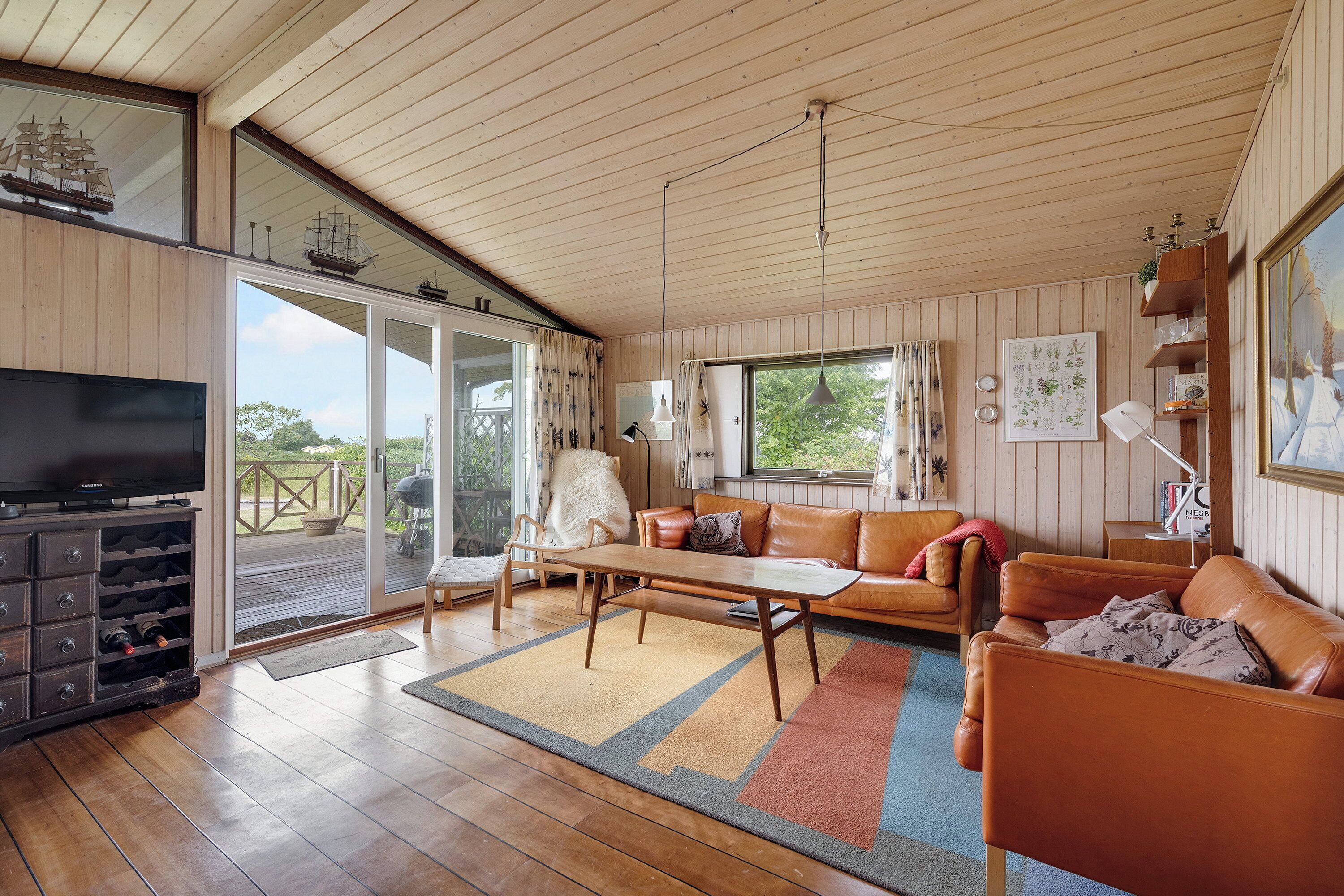 A spacious living room with a wooden ceiling, a television, a sofa, a coffee table, and a view through large glass doors.