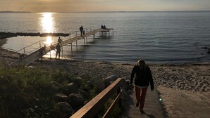 A beach with a wooden walkway leading to a pier, rocky shoreline, and a sunset over the water. - Beautiful sunsets 100 meters from the beach (Brenderup)