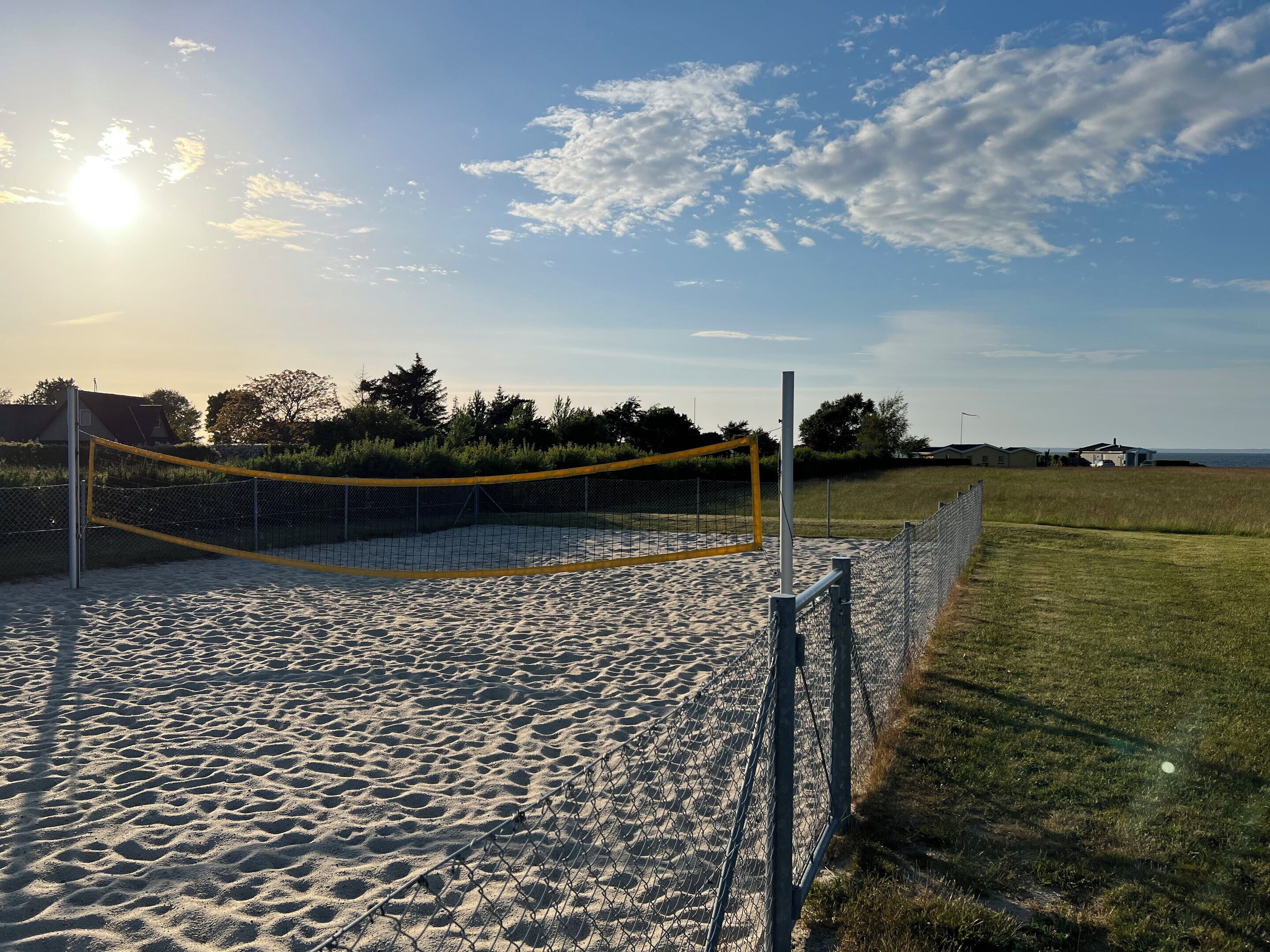 En sandvollybollplan med nät, omgiven av ett stängsel av kedjelänk och gräsområden.